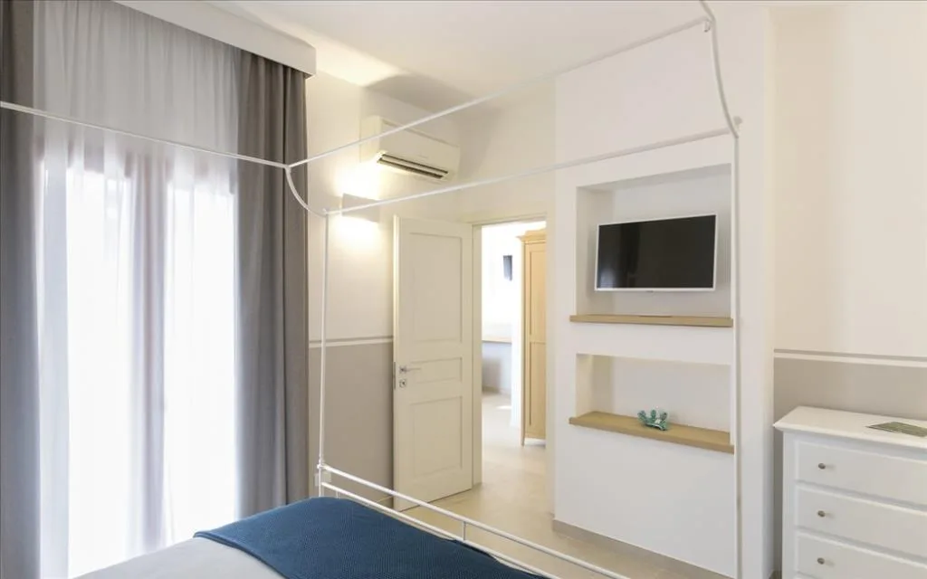 Camera con letto a baldacchino, TV a parete in nicchia, aria condizionata e cassettiera bianca