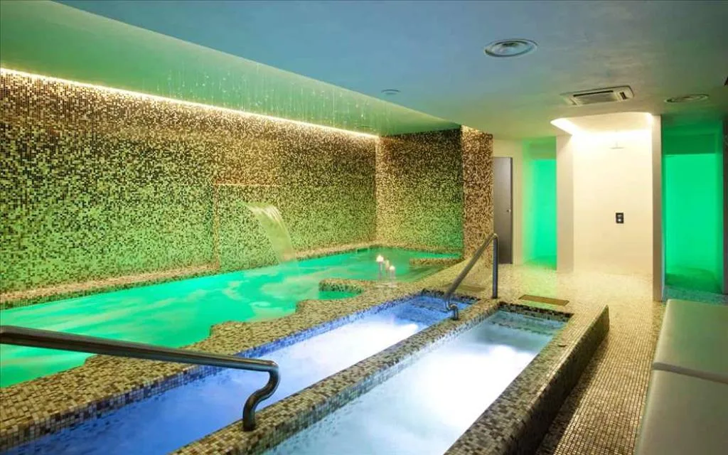 Piscina interna spa con mosaico dorato, cascata d'acqua e illuminazione verde suggestiva