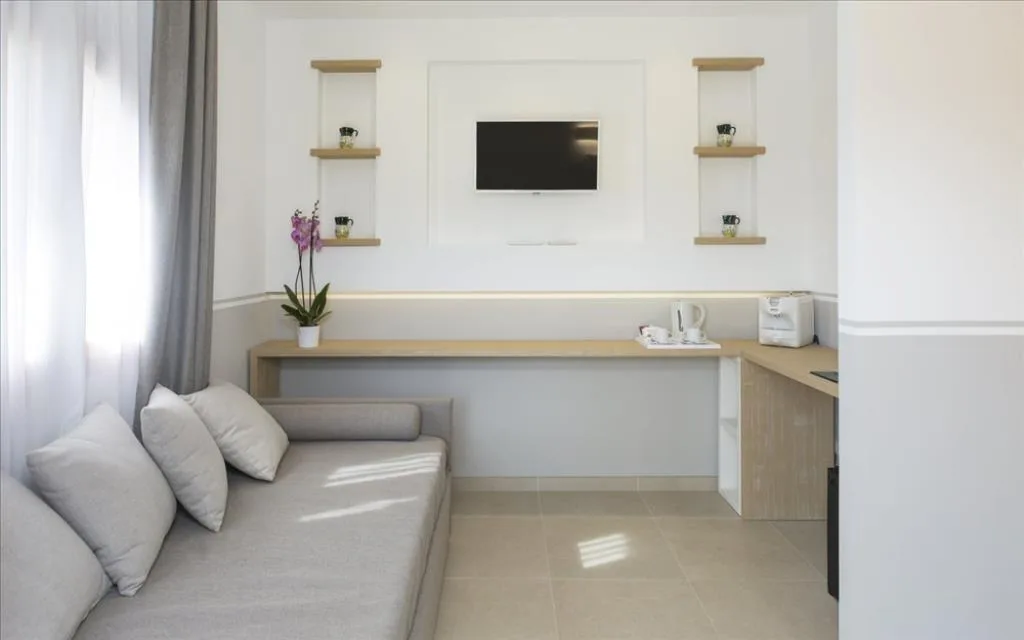 Soggiorno di camera con divano grigio, scrivania in legno, TV a parete e mensole decorative
