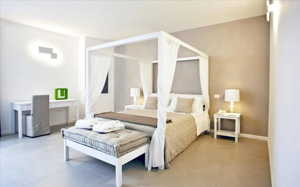 Camera spaziosa con letto a baldacchino bianco, scrivania, panca e comodini con lampade