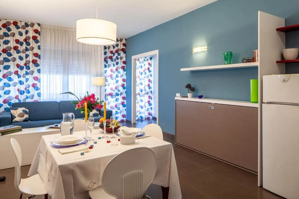Soggiorno luminoso con tavolo da pranzo apparecchiato, divano blu e parete azzurra con cucina
