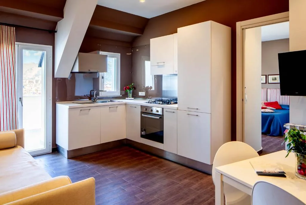Cucina con mobili bianchi, forno e piano cottura, affacciata su un soggiorno con divano blu