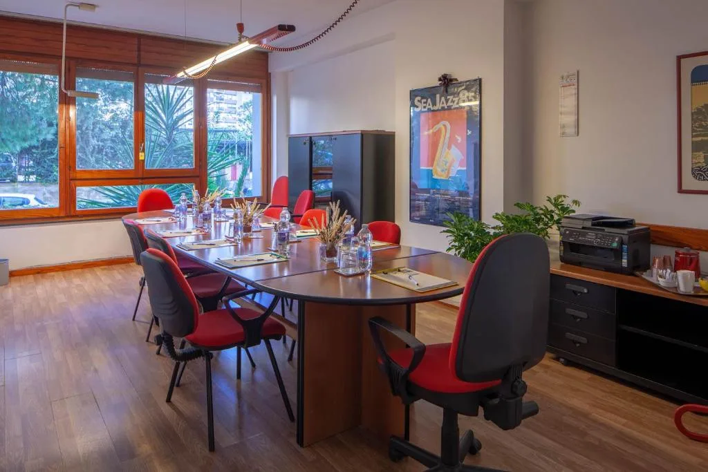 Sala riunioni con tavolo da conferenze, sedie rosse e nere e ampie finestre sul verde