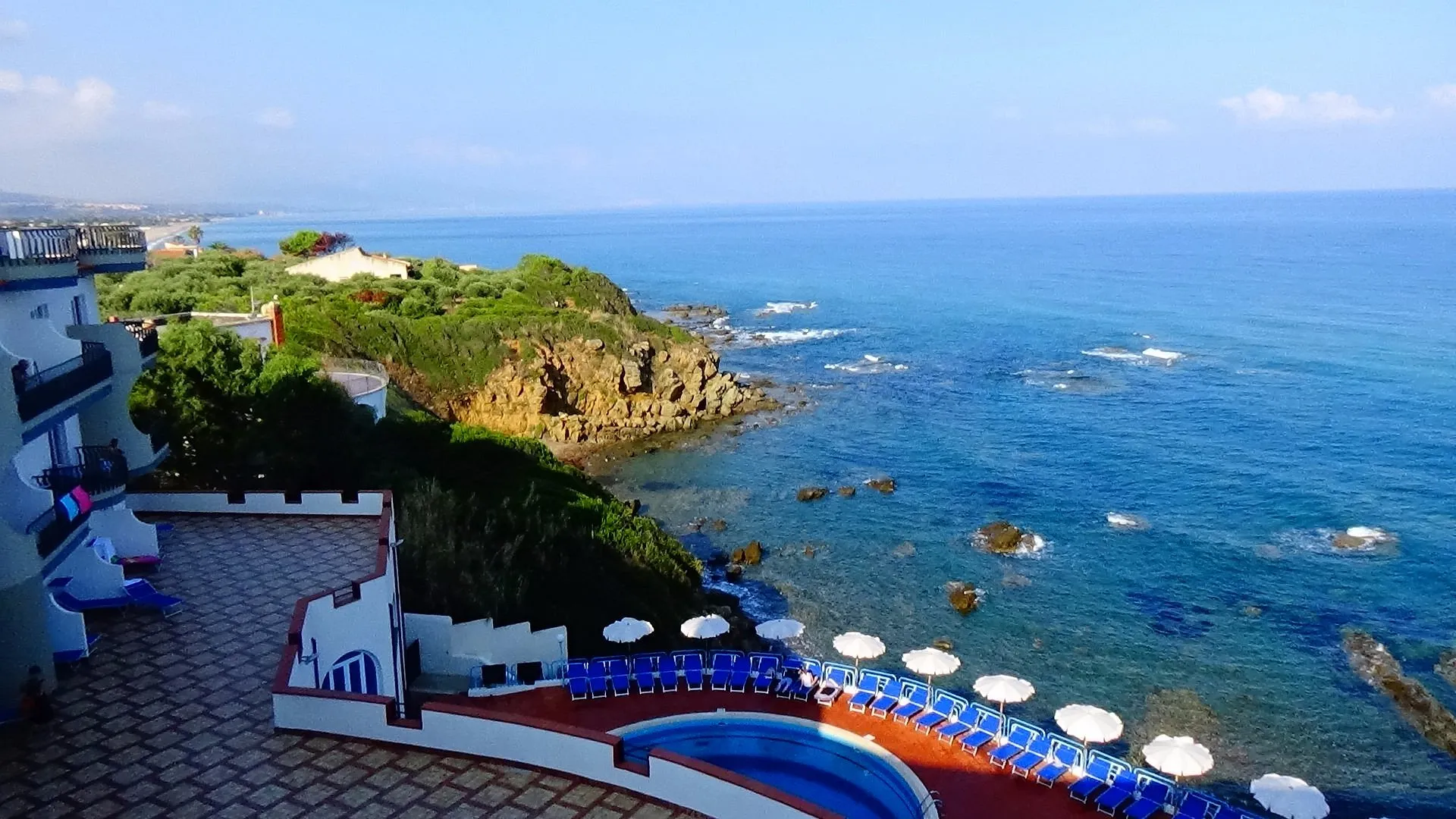 Vista panoramica sulla costa rocciosa e sul mare azzurro con lettini e ombrelloni sulla terrazza