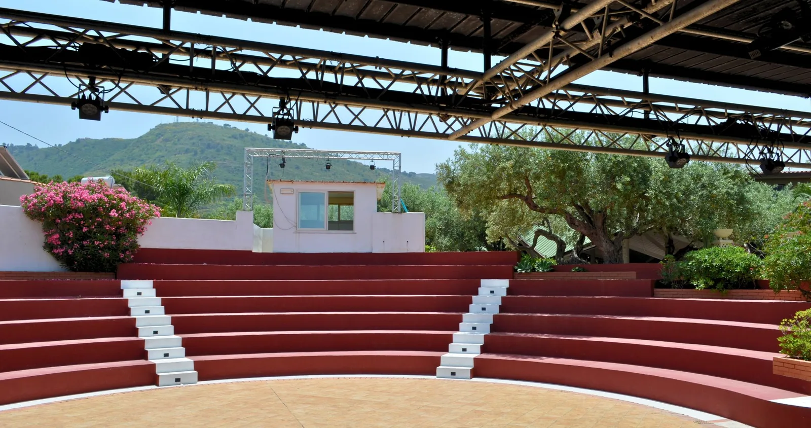 Anfiteatro all'aperto con gradinate rosse e palco coperto immerso nel verde e nelle colline
