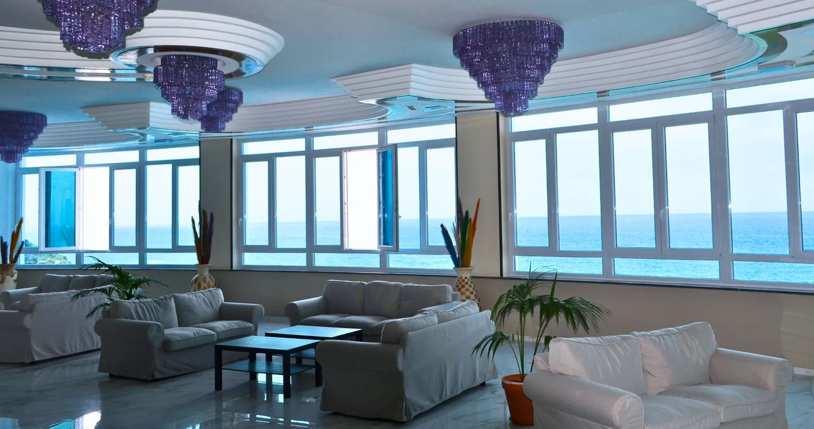 Hall dell'hotel con divani bianchi, lampadari viola e ampie vetrate affacciate sul mare