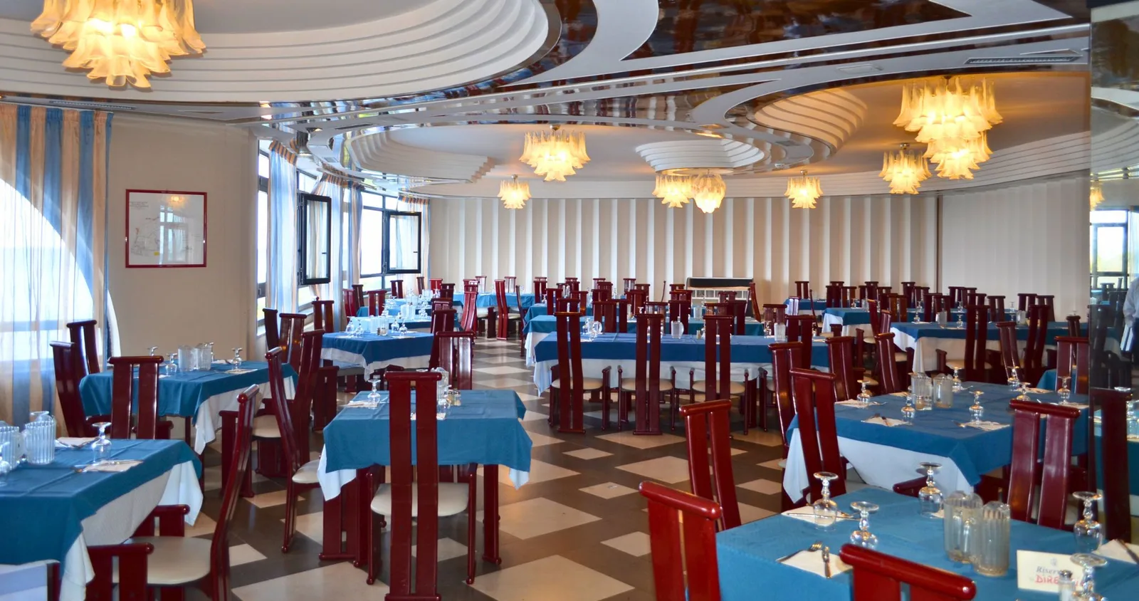 Sala ristorante interna con tavoli apparecchiati, tovaglie azzurre e lampadari eleganti