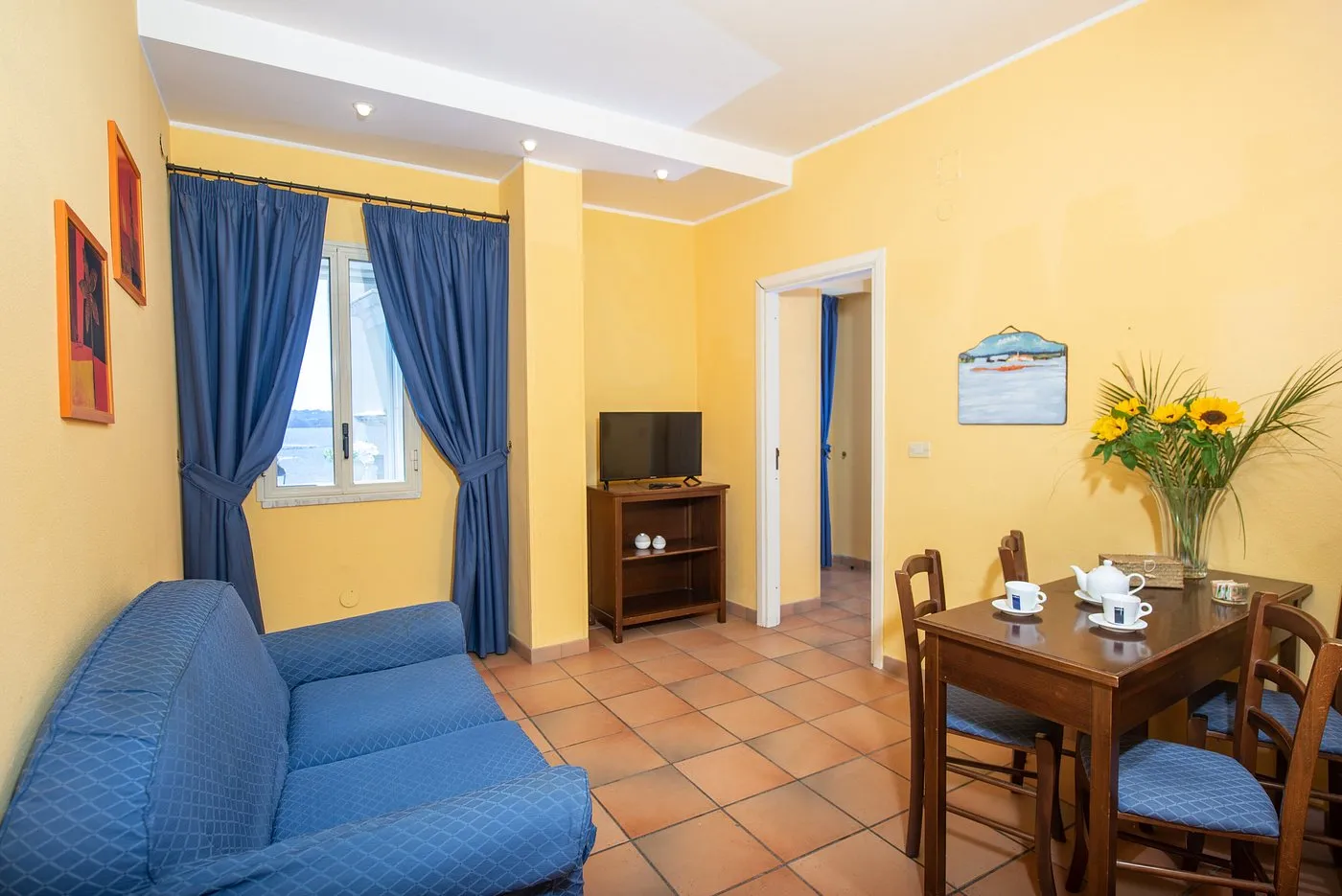 Soggiorno luminoso con divano blu, tavolo in legno e finestra con vista mare