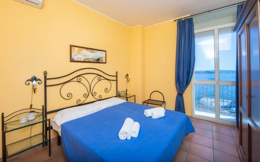 Camera matrimoniale gialla con letto in ferro battuto e finestra con vista mare