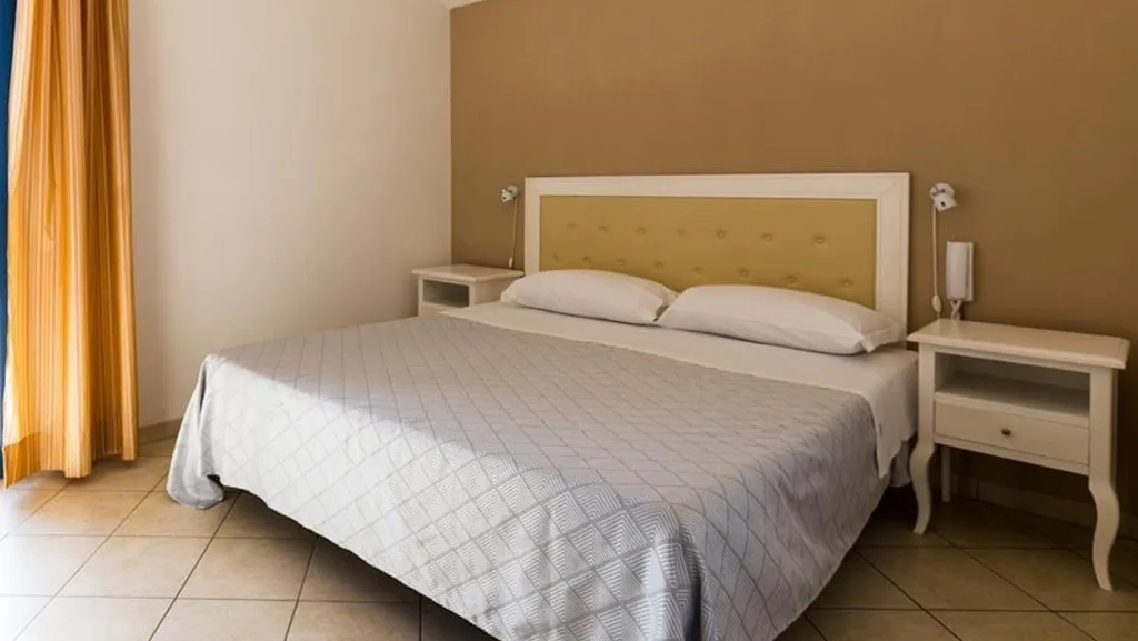 Camera con letto matrimoniale, testiera imbottita beige e comodini bianchi