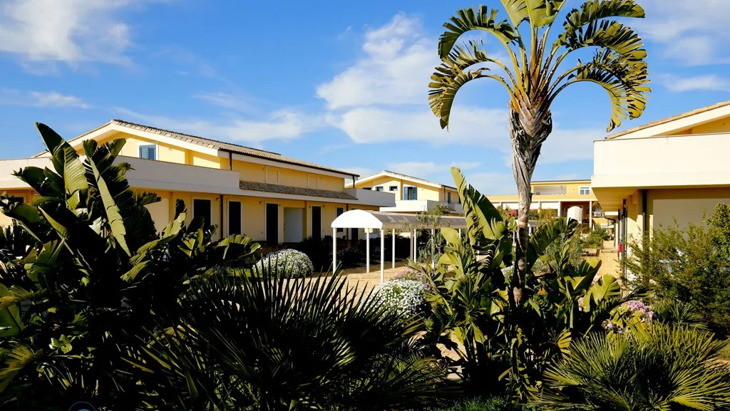 Esterno del residence con villette gialle, palme e vegetazione mediterranea