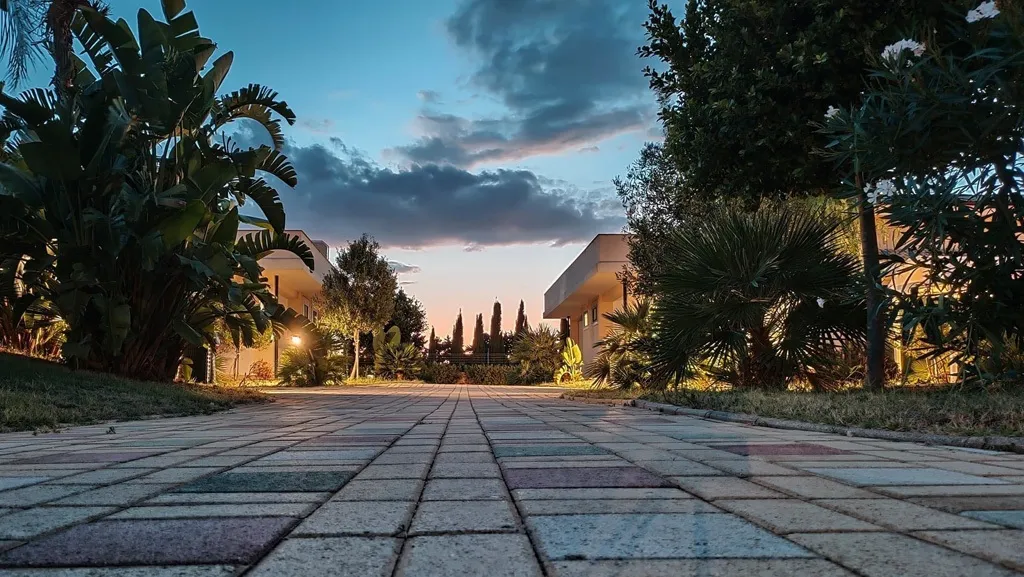 Vialetto pavimentato del residence al tramonto tra palme e vegetazione