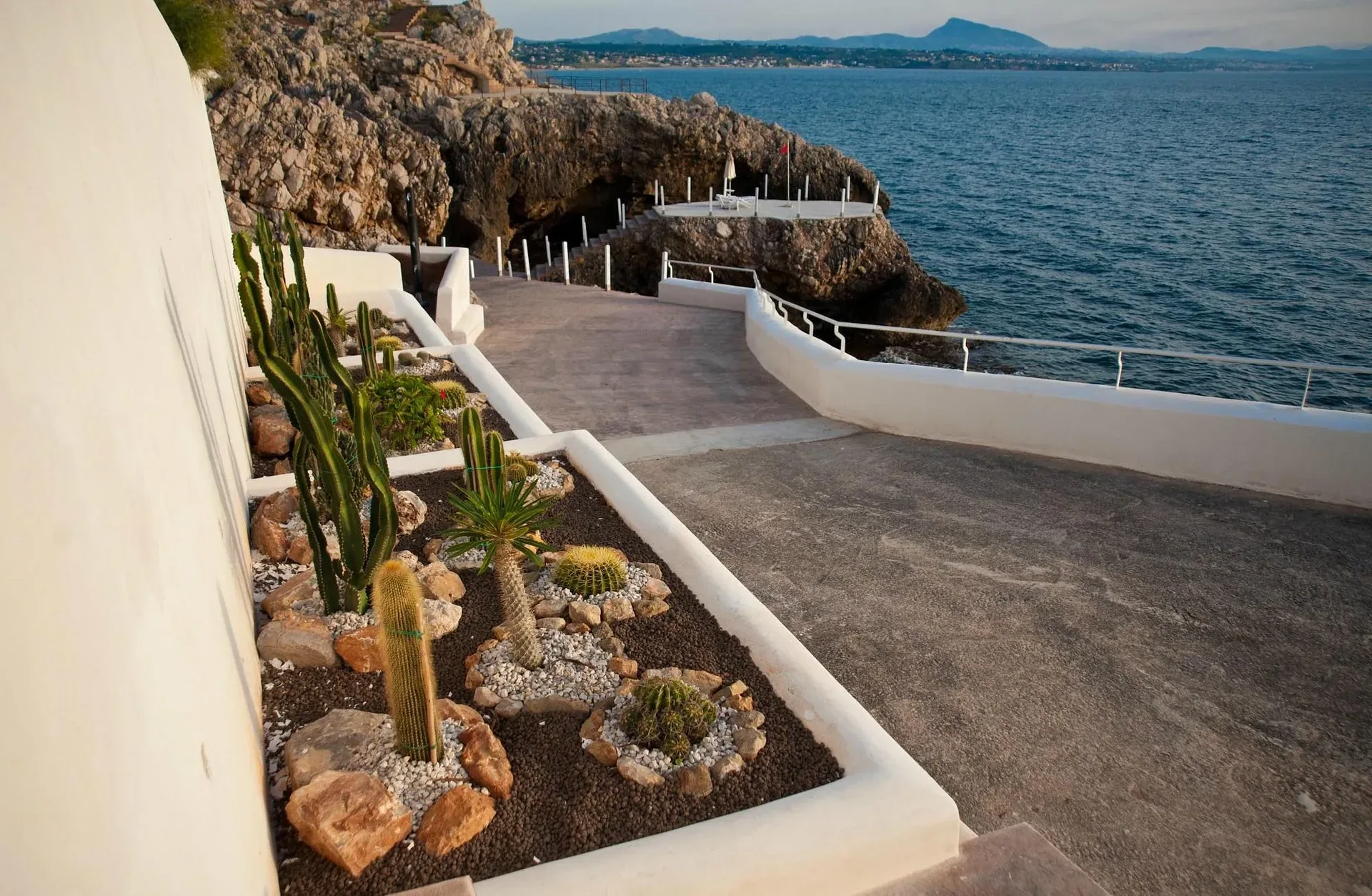Camminamento bianco a picco sul mare con giardino di cactus e piante grasse