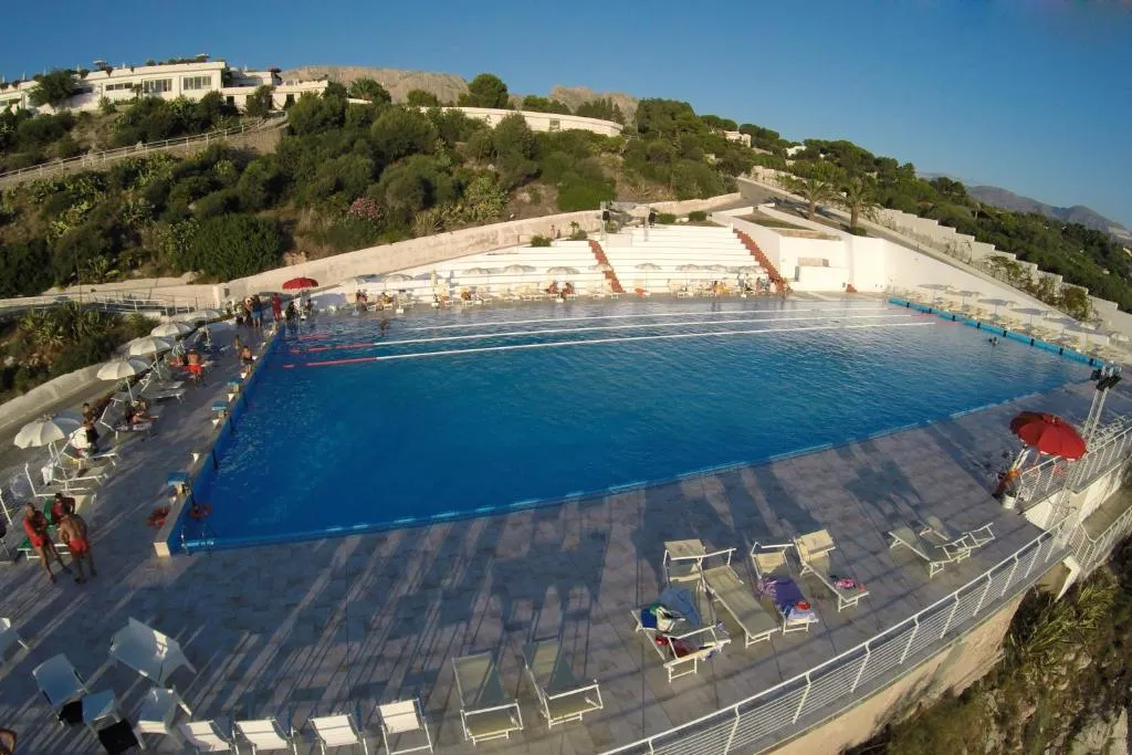 Ampia piscina con lettini e ombrelloni immersa nel verde della collina