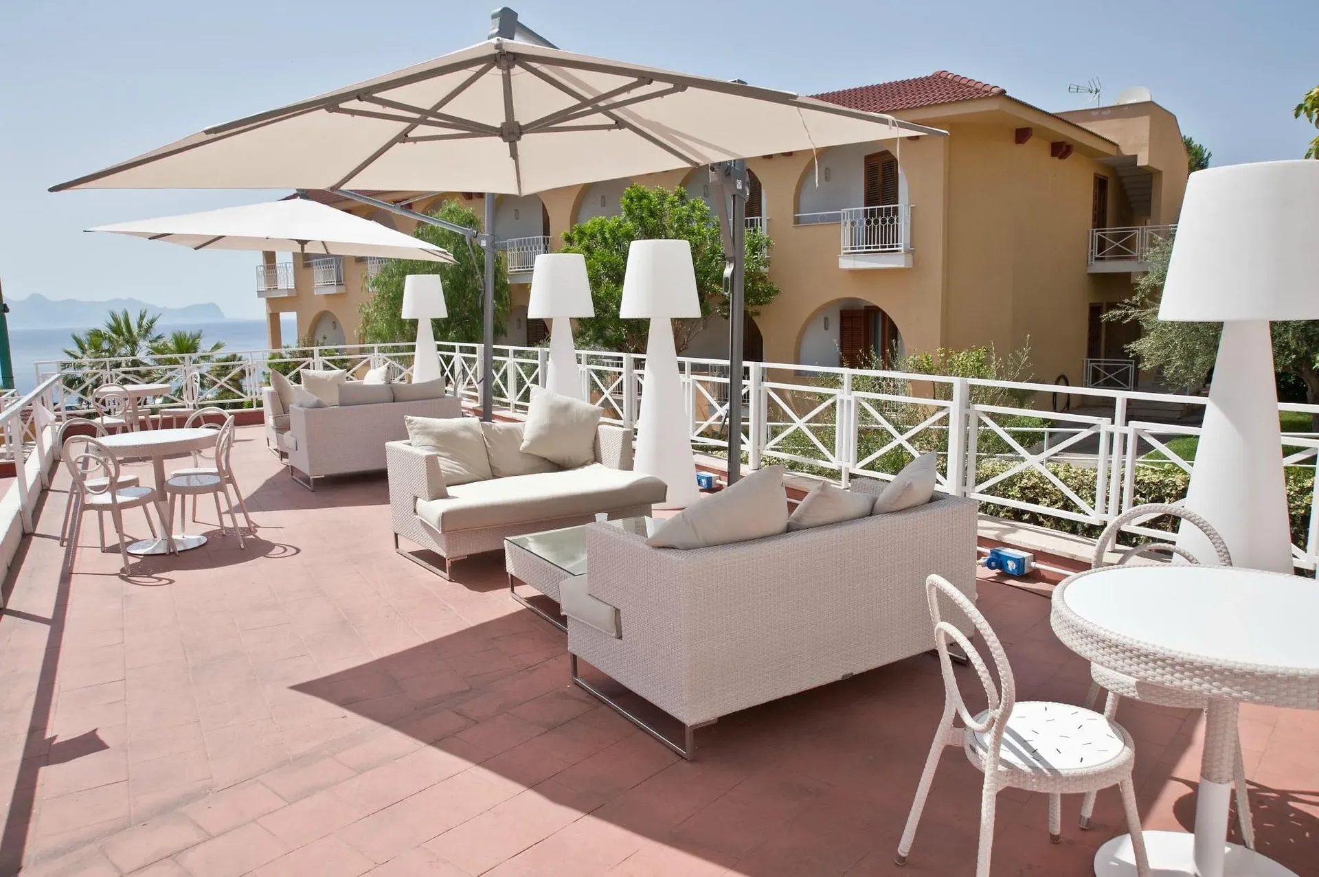 Terrazza lounge con divani, ombrelloni e vista mare accanto agli edifici del resort