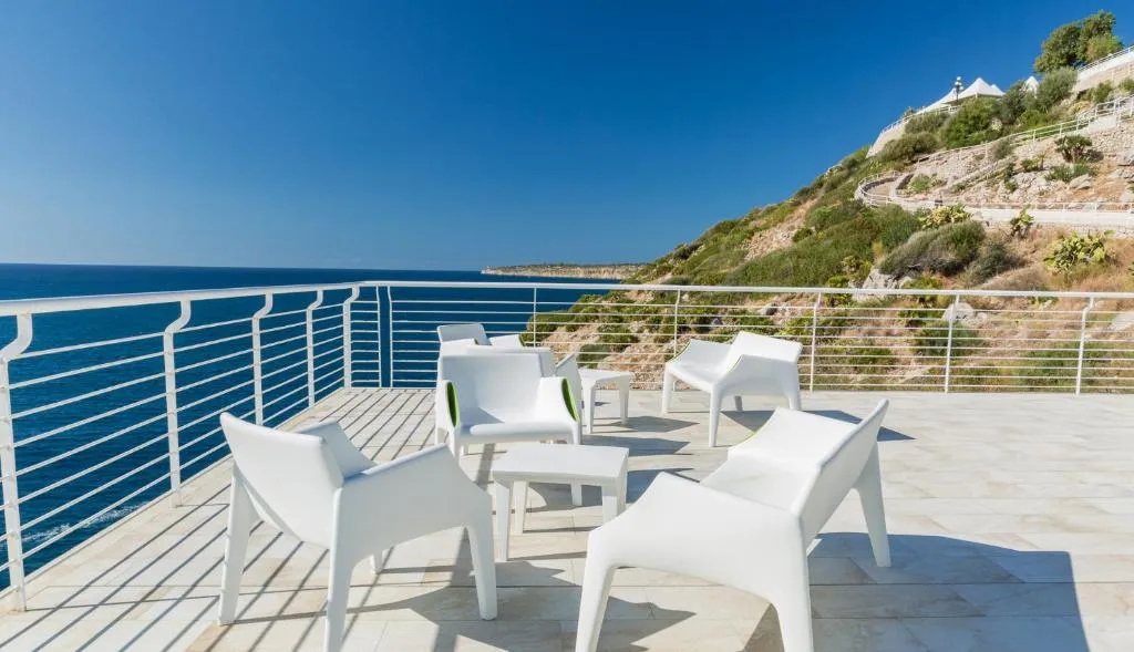 Terrazza con poltrone bianche affacciata sul mare e sulla costa rocciosa